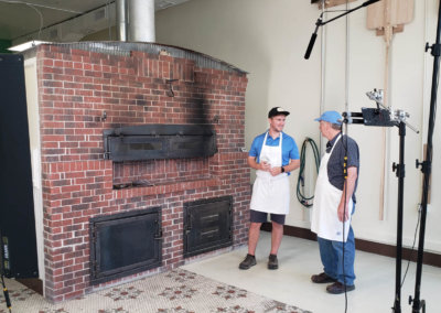 2 people standing in front of a giant brick oven