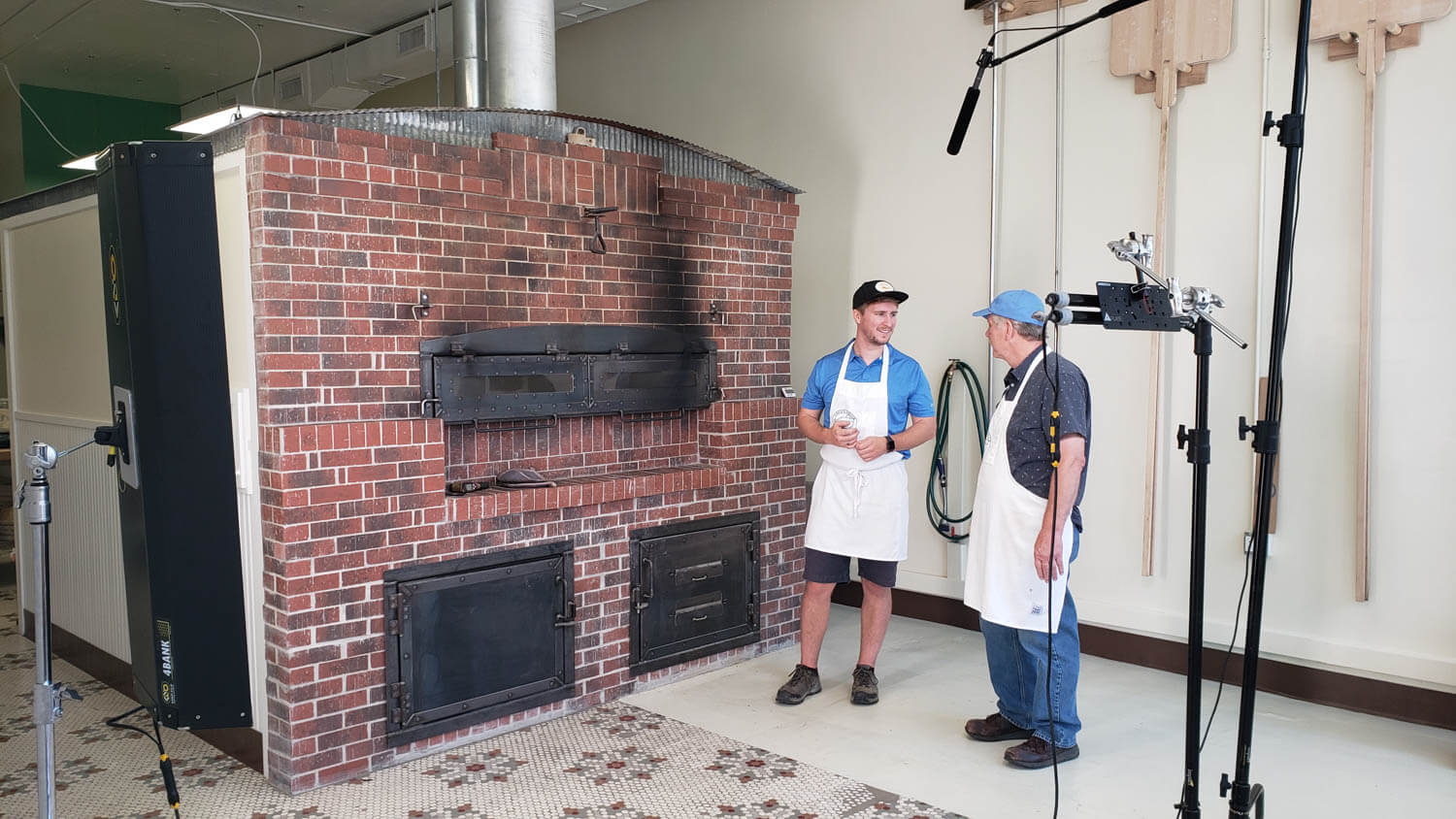 2 people standing in front of a giant brick oven